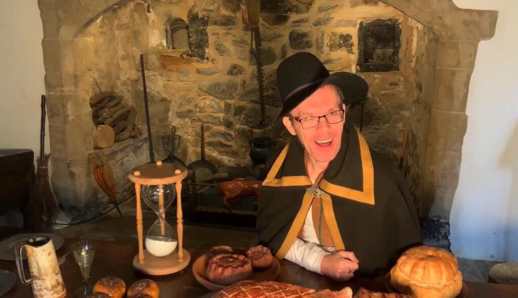 Image of a white middle aged man in a costume smiling at the camera, surrounded by props.