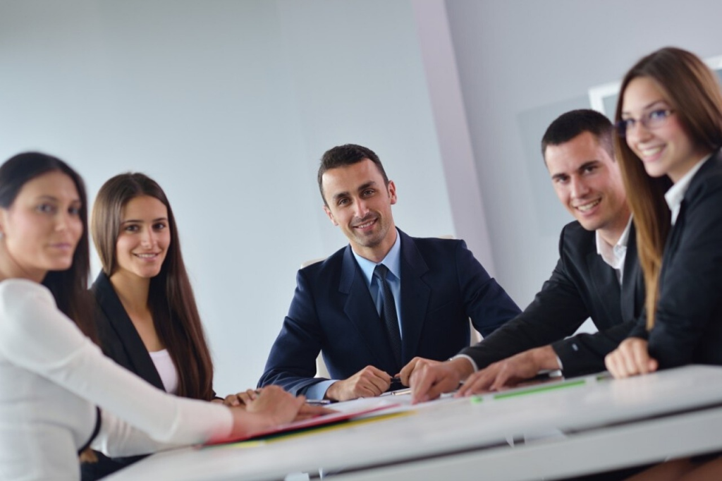 An image of five adults around a table in suits and smart clothes facing the camera and smiling.