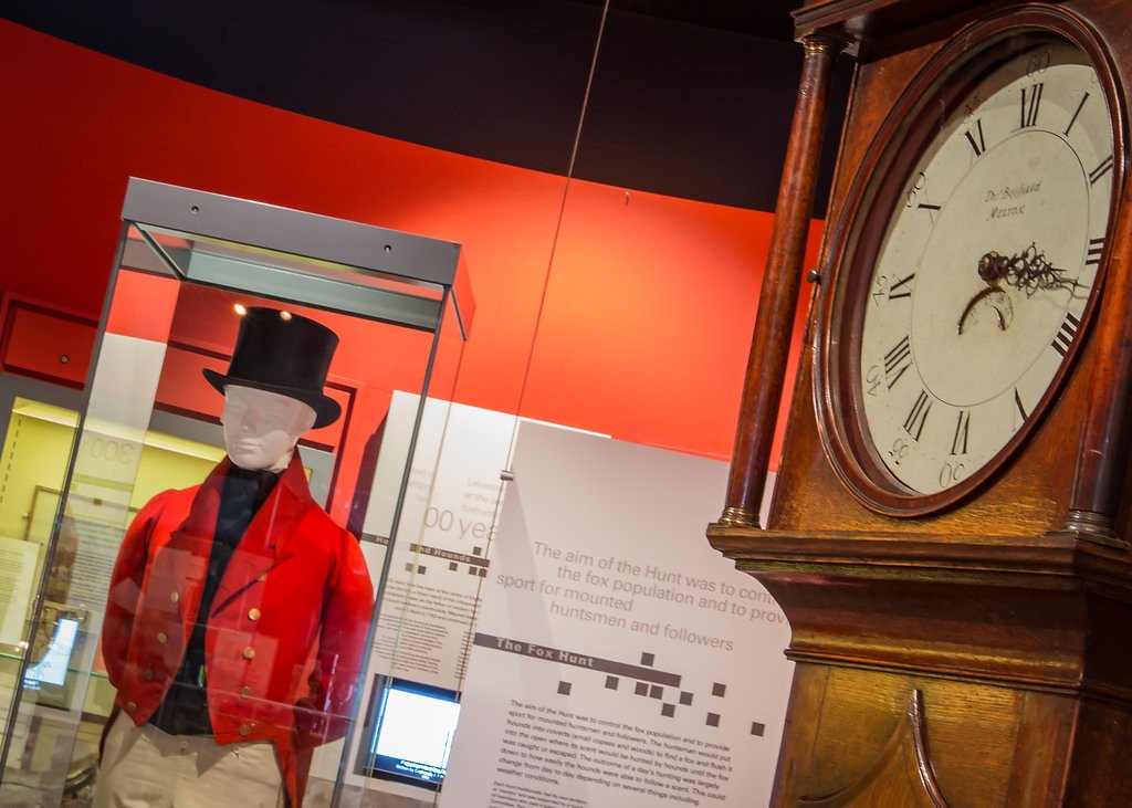 Museum gallery with mannequin in a red jacket and top hat alongside a grandfather clock.