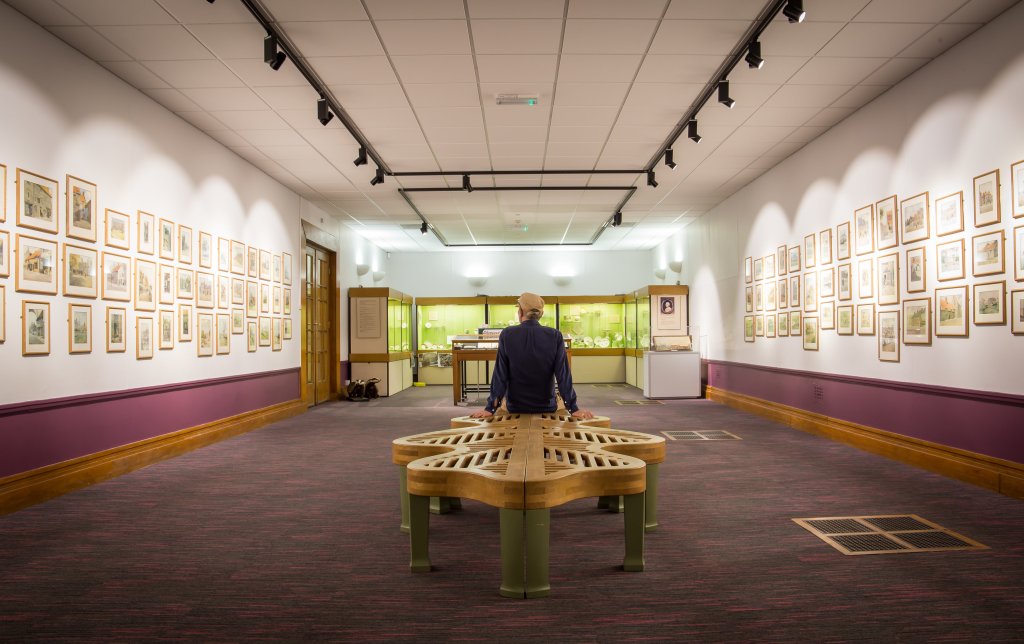 Man sat on wooden bench in a museum gallery.