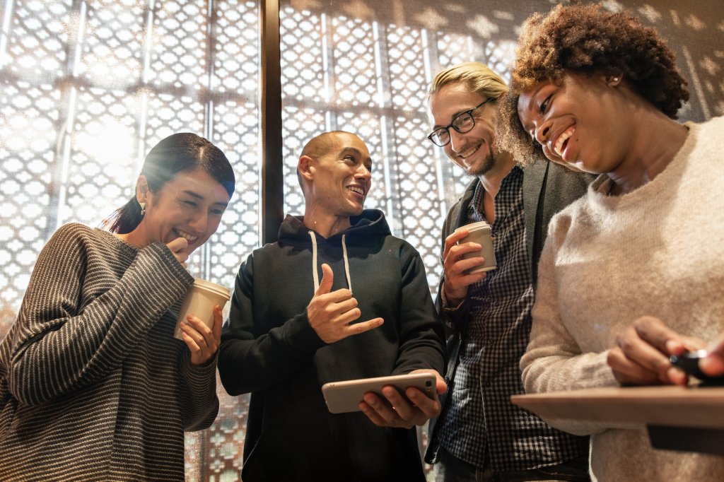 Four happy people standing looking at a a mobile screen.