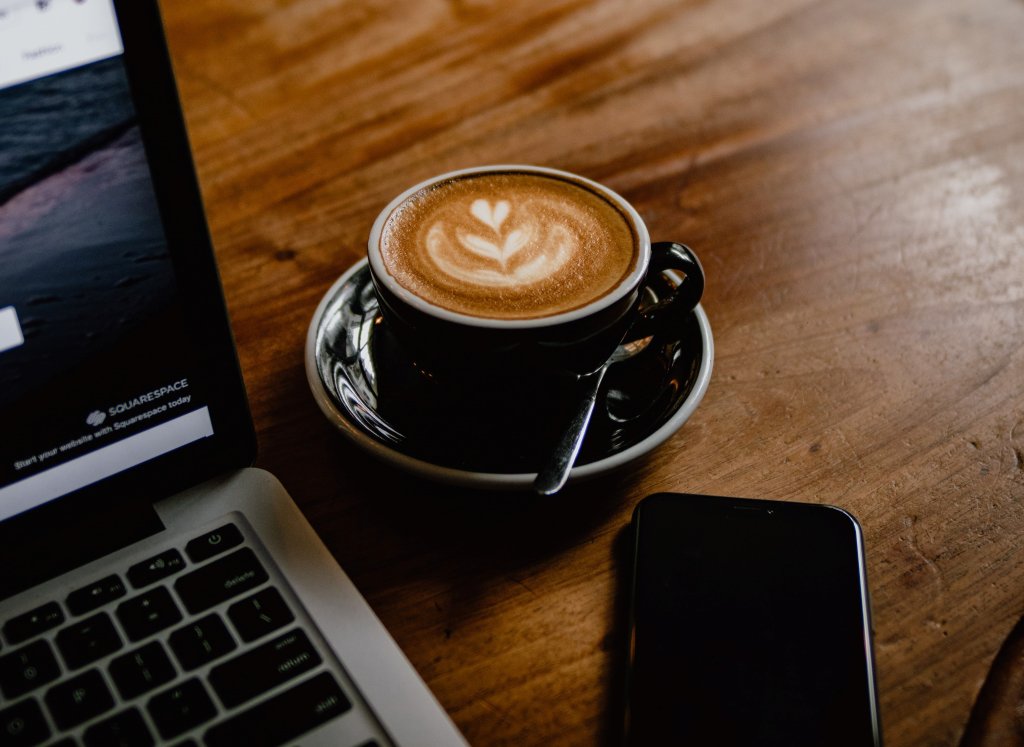 Cup of coffee by a laptop and mobile phone.