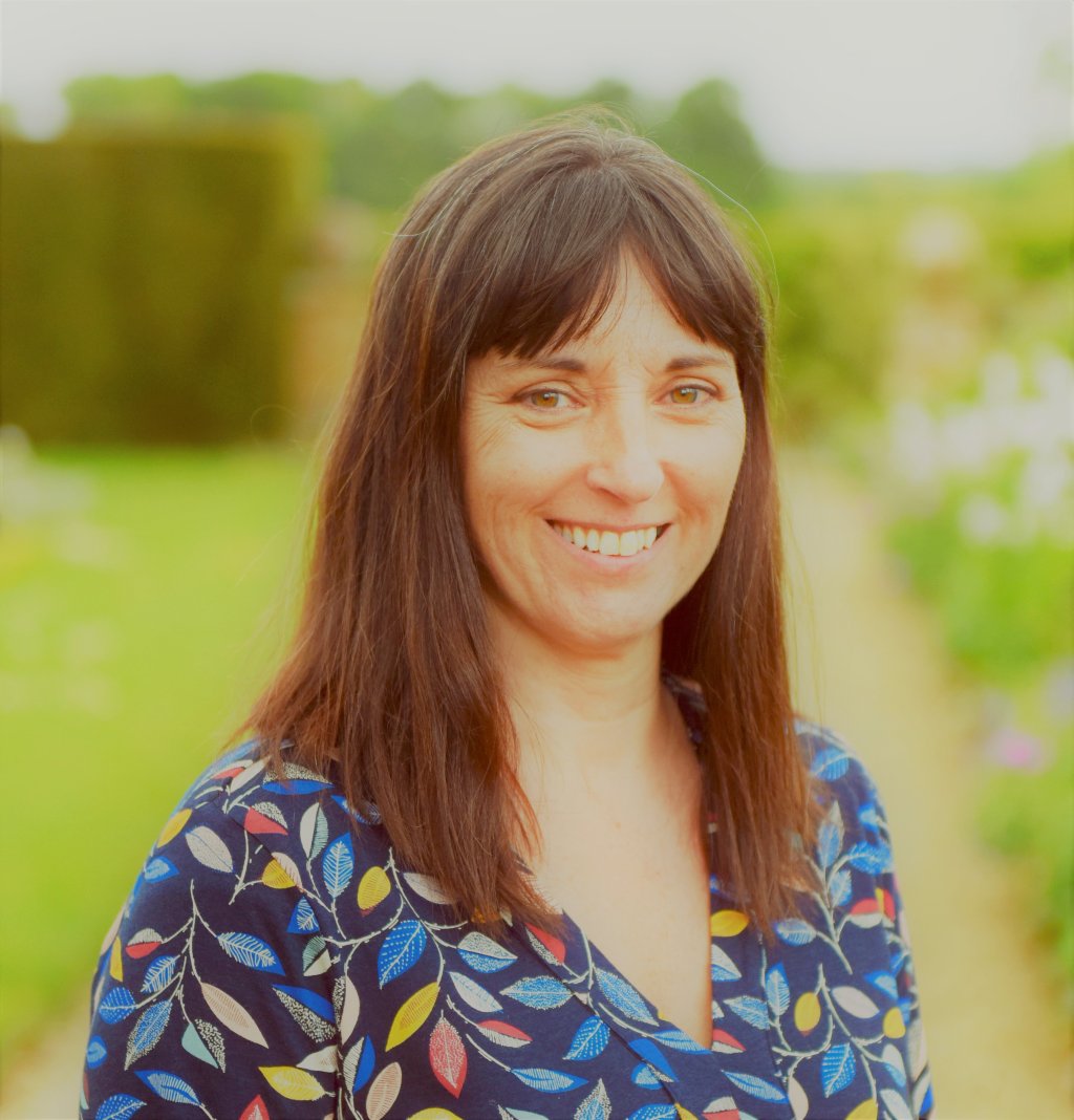 Head shot of Alison Ray she has shoulder length straight brown hair and is wearing a blue floral patterned blouse.
