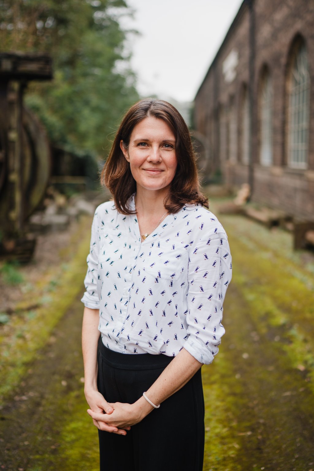 Woman with brown hair wearing a white and blue blouse and a dark skirt outside an old building.
