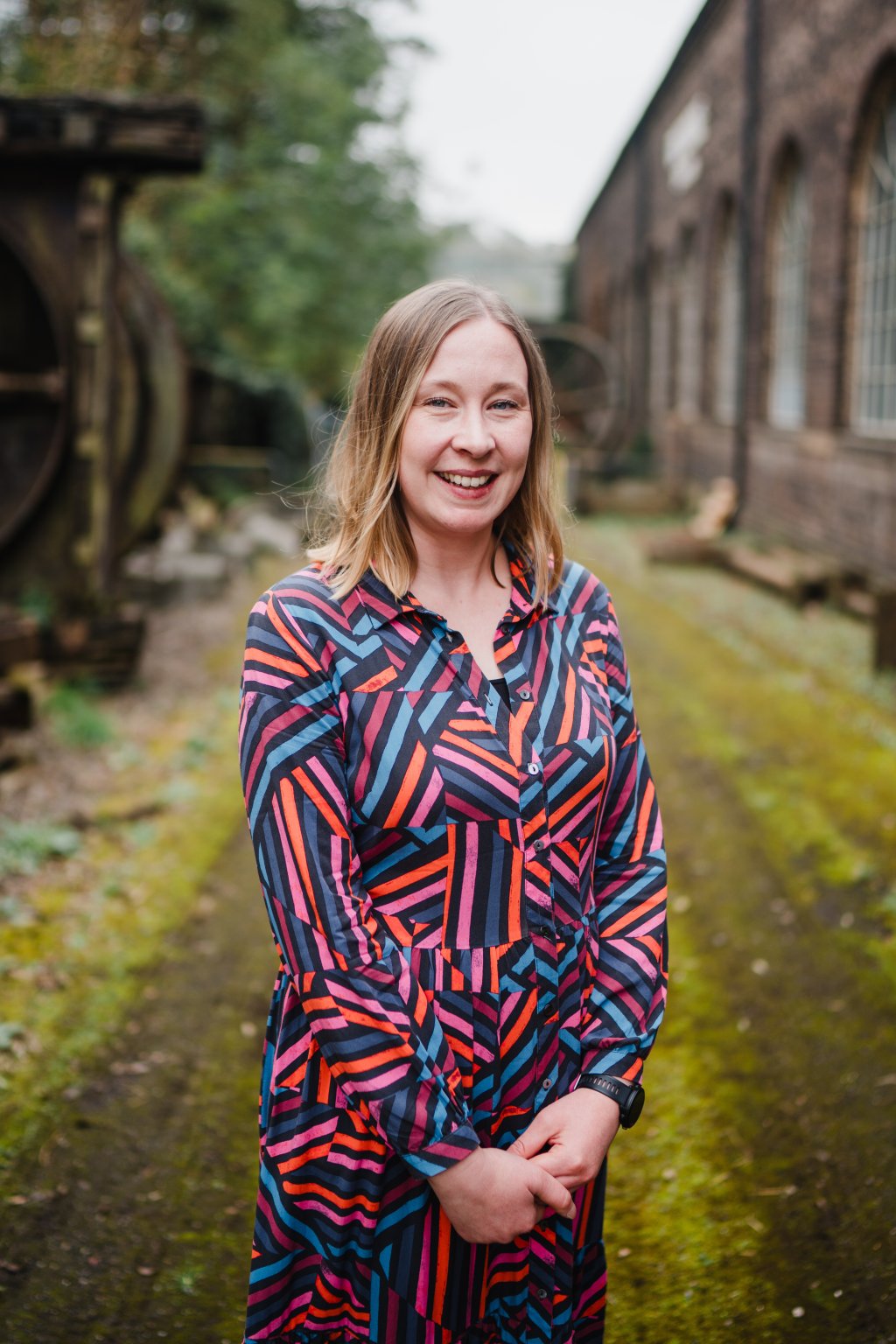 Woman with light blond hair wearing a multicoloured dress outside an old building.