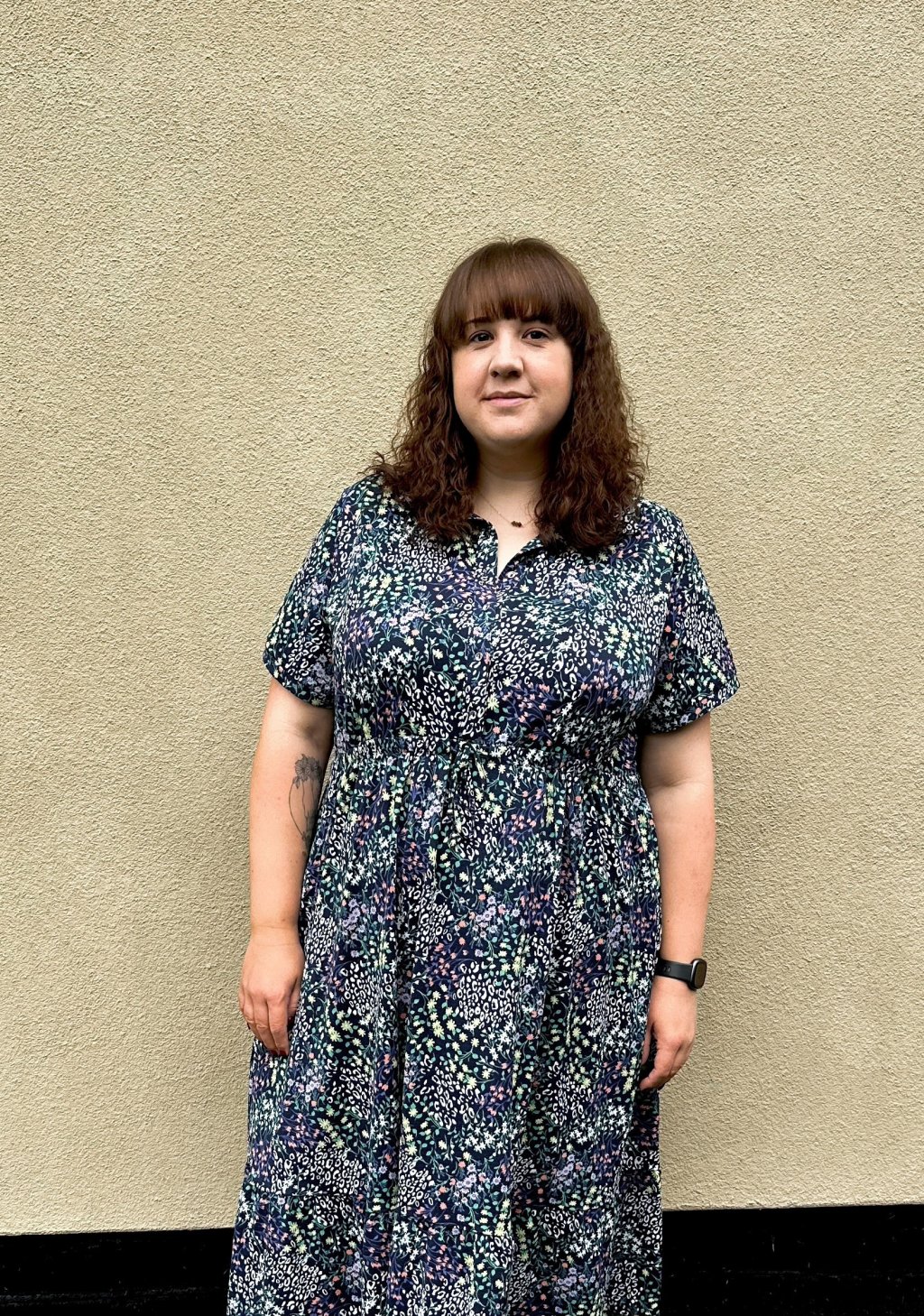 Sally standing in front of a cream wall in a black and white patterned dress.