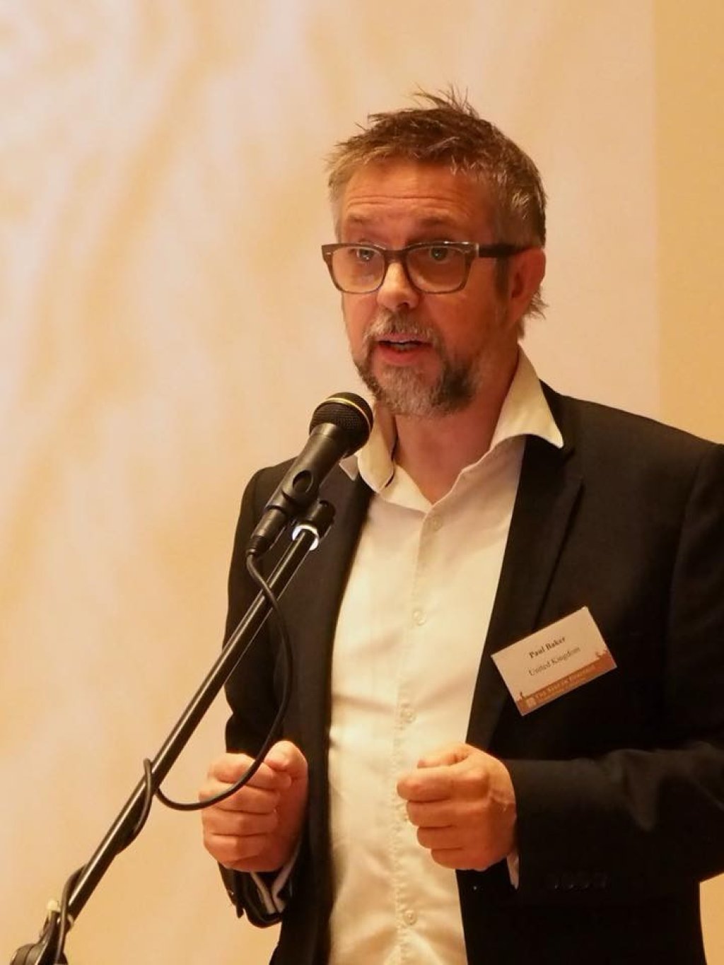 Man with beard and glasses speaking into a microphone.